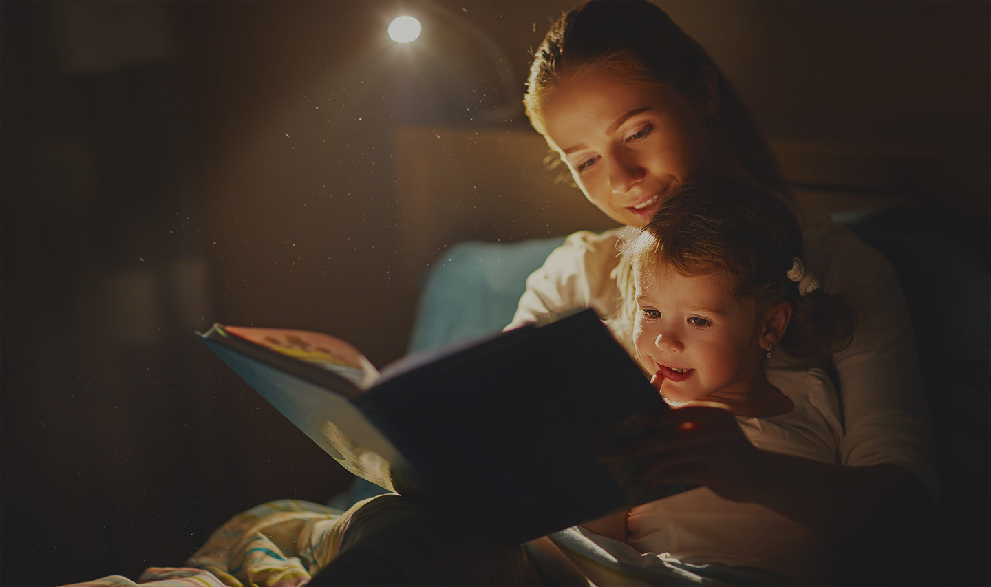 A woman reading a book to her child at bedtime. 