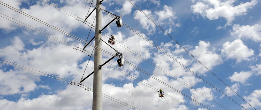 ground up view of a transmission line with white clouds in a blue sky background